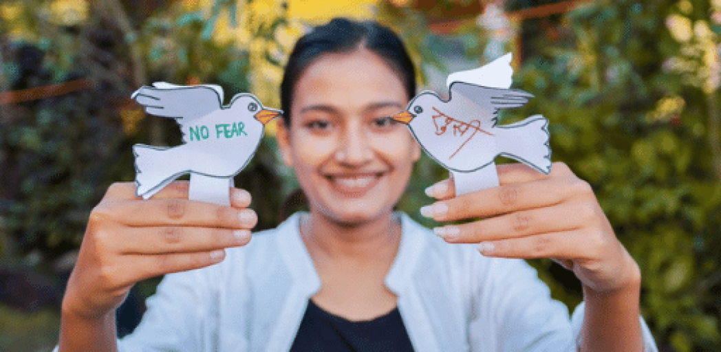 Young woman with dark hair and light brown skin holds her hands out with a paper dove resting on each finger