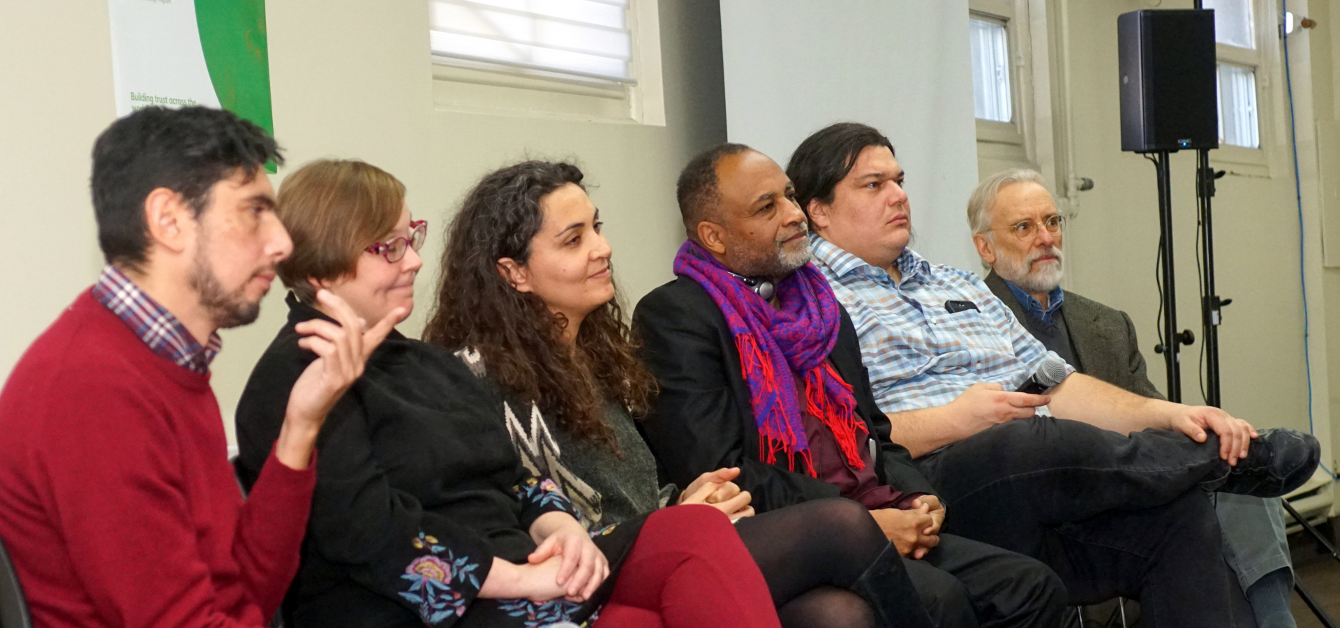 Six panelists, of different ages, genders, and ethnicities, look out over crowd of attendees,
