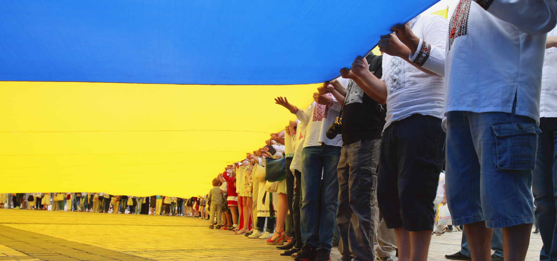 Ukrainians hold a vast flag at a patriotic ceremony.