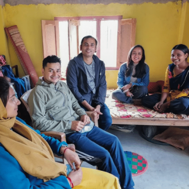 Two young Nepalese males and three females gather in a small, brightly colored room to talk about trust