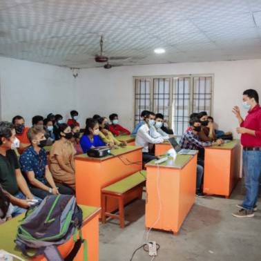 A Nepalese facilitator in a red shirt looks out over a classroom full of Nepalese youth 