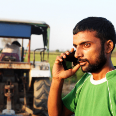 Southeast Asian male with short dark hair speaks on mobile phone with tractor parked in the background